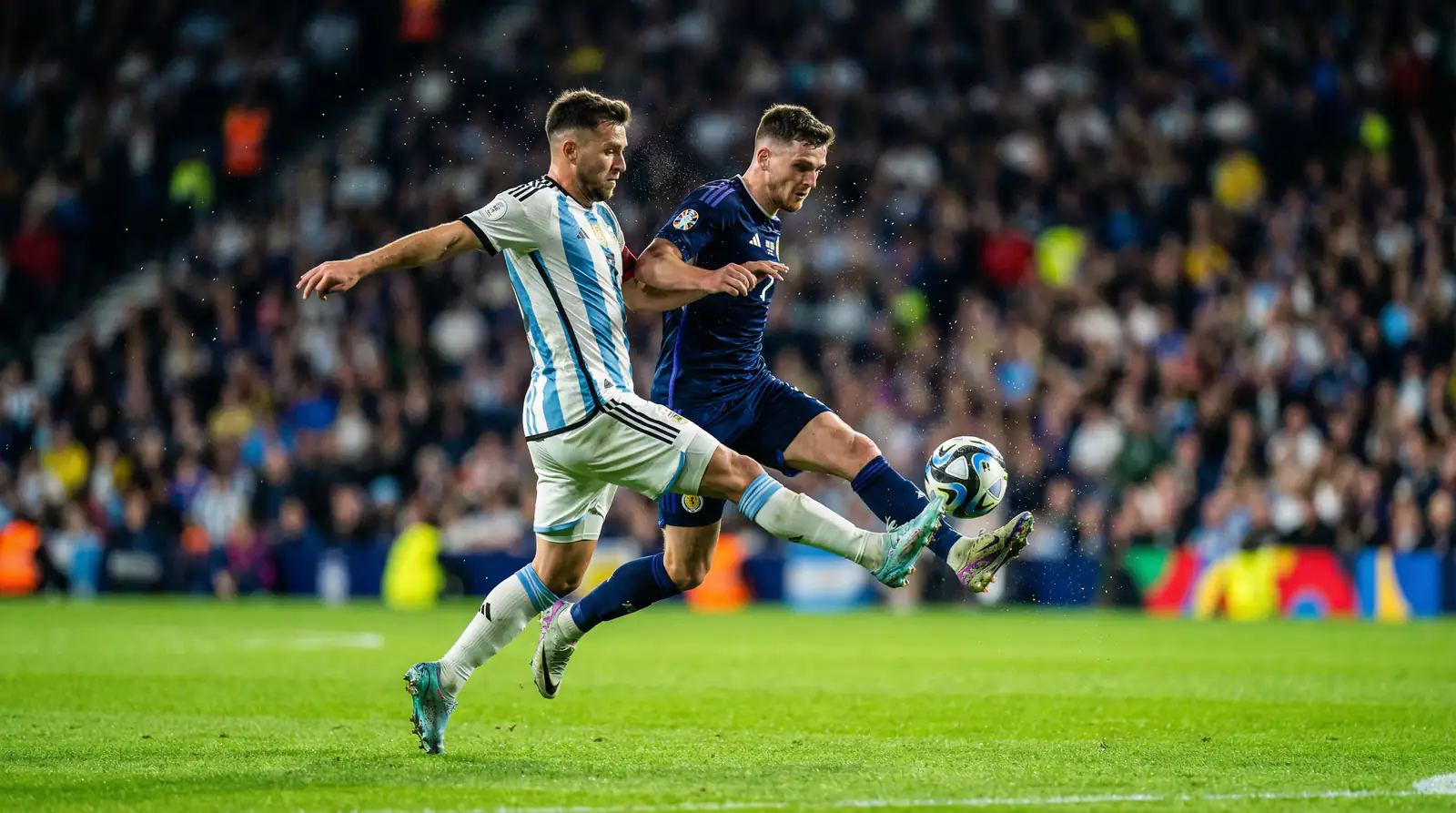 Fotbollsspelare i aktion under en internationell turnering med fullsatta läktare i bakgrunden